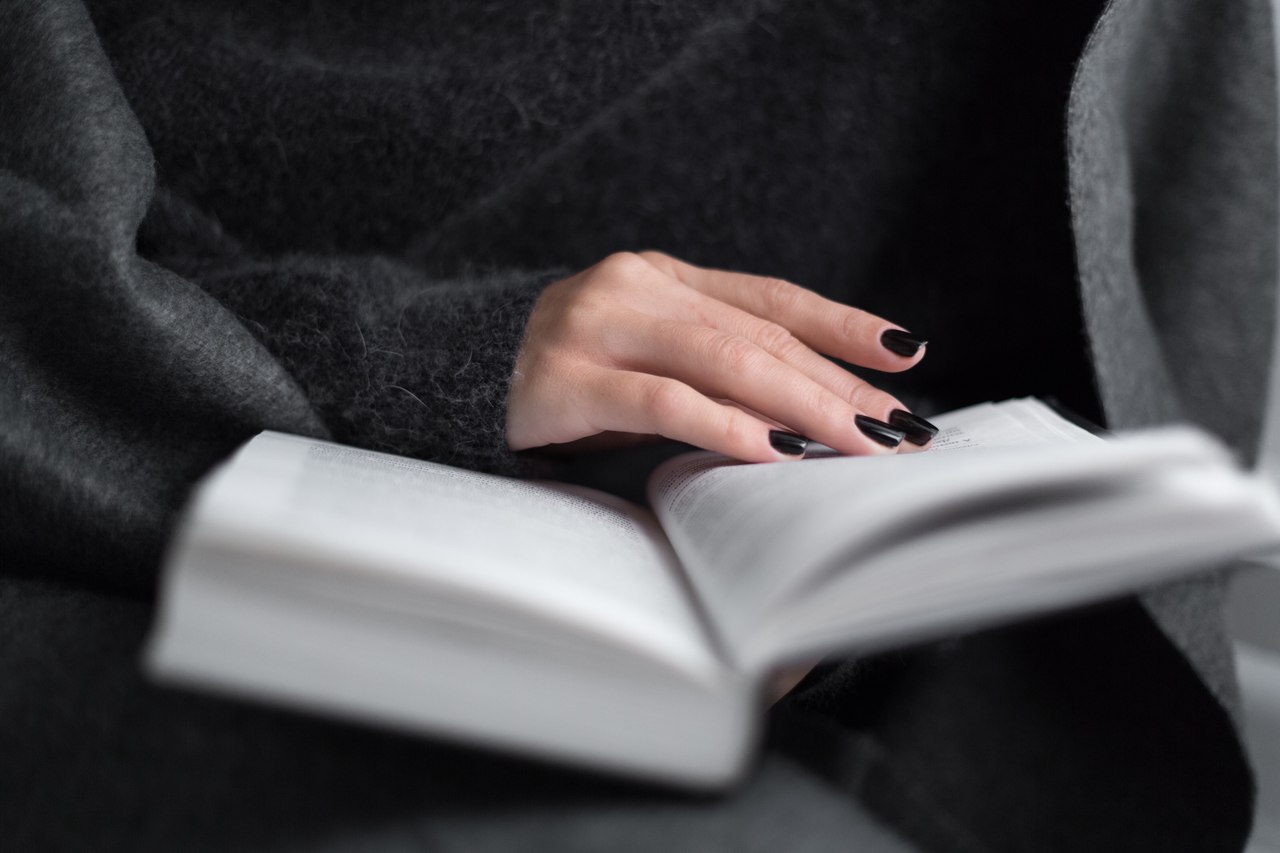 kitap okuyan ve ellerinde siyah ojeler bulunan bir kadın görseli